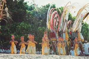 Kure Beach, NC, Camping And Hiking Tours 6 Traditional dancers in colorful ceremonial clothing performing on a sandy beach with tall decorative banners.