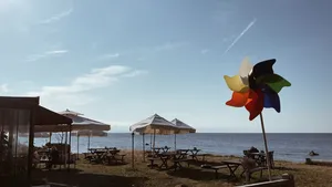 Kure Beach, NC, Camping And Hiking Tours 5 Seaside outdoor dining area with picnic tables, umbrellas, and a colorful pinwheel overlooking the ocean.