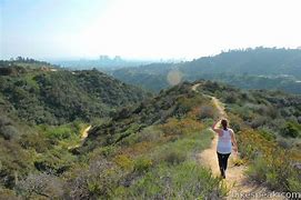 Person walking on a trail in a canyon mountainous area with green vegetation and a hazy day.