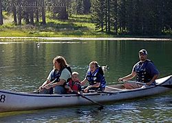 People canoeing with life jackets on a lake with trees in the background.