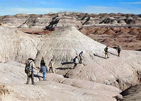 People Hiking some wearing backpacks in a canyon that's hilly on a partly cloudy day.