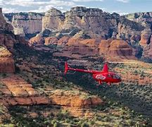 Helicopter tour at a canyon with green vegetation and clor canyon walls and steep cliffs on a partly cloudy day.