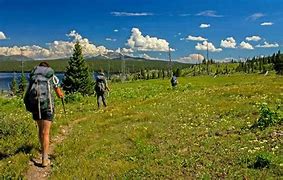 People hiking on a path with backpacks near trees in a flat field on a partly cloudy day.