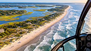 Fish Haul Beach SC Camping and Hiking Tours 7 Aerial view from a helicopter overlooking a beautiful coastal beach, rolling ocean waves, sandy shoreline, lush green marshlands, winding waterways, and coastal homes beneath a clear blue sky.