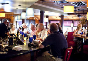 Lighthouse Inlet Beach, SC, Camping and Hiking Tours 8 Guests enjoying food, drinks, and conversation inside a lively restaurant featuring a modern bar, blue drinking glasses, colorful pendant lighting, and comfortable seating.