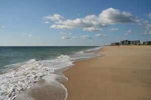 Sandy beach with gentle waves and a distant building overlooking the coastline.