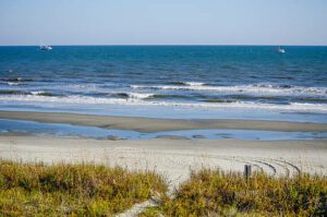 Sandy beach with gentle ocean waves rolling onto the shore under a clear sky.