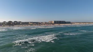 Wide ocean view with rolling waves approaching a sandy Carolina beach lined with beachfront buildings under a clear blue sky.
