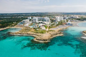 Aerial view of a seaside resort surrounded by rocky coastline, sandy beaches, palm trees, and clear turquoise ocean water.