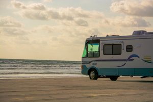 Isle of Palms, South Carolina: Beach Camping Getaways, Coastal Adventures & Scenic Escapes 2 A large white and teal motorhome parked on a sandy beach overlooking the ocean, with gentle waves rolling onto shore beneath a warm, cloudy sky.