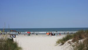 Pathway leading to a sandy beach crowded with people enjoying the ocean.
