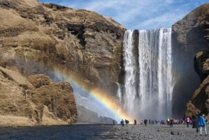 Waterfalls with people near a river and steep cliffs and a rainbow.