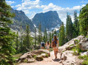people hiking on a path in a forest on a hill with mountains
