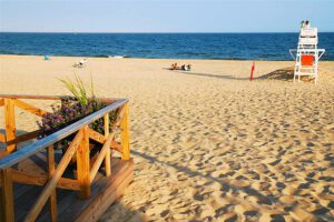 🌞🌴⛱️🐚Beach Camping & Hiking: 25 Top Coastal Spots in North & South Carolina🏊♀️🏄♂️🤿✈️ 1 View from a balcony overlooking a sandy beach, ocean waves, and a lifeguard station under a clear sky.