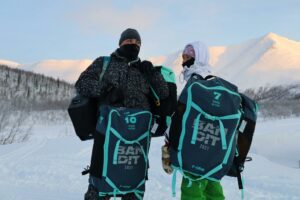 two people wearing jackets and hats in the winter with backpacks hiking