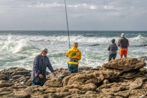 people fishing in the ocean on rocks