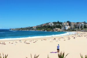 People on a beach near the ocean in Australia with buildings on a hill in the background