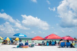 people at the beach sitting in chairs with umbrellas and laying on blankets near the ocean on a partly cloudy day