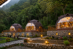 Luxury glamping domes nestled against a lush mountain rainforest, featuring illuminated interiors, stone terraces, wooden decks, landscaped gardens, and scenic wilderness surroundings.