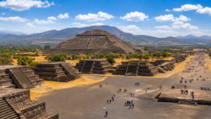 Panoramic view of the Pyramid of the Sun at Teotihuacan, Mexico, featuring the Avenue of the Dead, ancient stone temples, visitors exploring the archaeological site, and distant mountains beneath a bright blue sky.