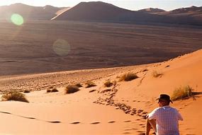 person sitting on a hill in a desert with mountains at a distsance.