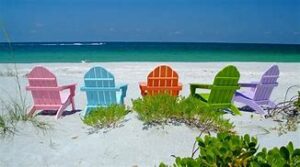 A sandy beach with chairs of different colors next to the ocean.
