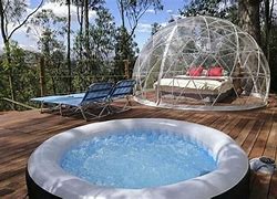 Glamping see through structure and a spa with lawn chairs and trees in a woods.