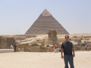 Traveler standing in front of the Sphinx with the Great Pyramids of Giza in the background, Egypt.