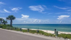 Casey Key: Secluded Old-Florida Charm On The Gulf Coast 2 Beach with parking lot with a post fence and a sandy beach next to the ocean on a partly cloudy day.