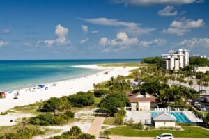 Longboat Key: Tranquil Beaches & Upscale Charm on Florida’s Gulf Coast 1 Beachfront resort with palm trees, a swimming pool, and buildings along a sandy shoreline beside the ocean.