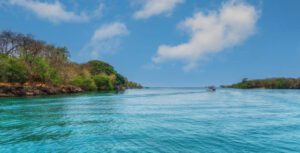 Isla Grande, Rosario Islands, Colombia: Tropical Beachfront Glamping Escape✨ 1 Blue ocean with land and trees in a forest and a boat.