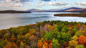 Forest with leaves changing colors in the fall at lake with a partly cloudy sky.