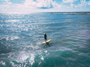 Longboat Key: Tranquil Beaches & Upscale Charm on Florida’s Gulf Coast 7 Person stand-up paddleboarding on sparkling blue coastal waters under a partly cloudy sky, with a long rock breakwater visible in the distance.