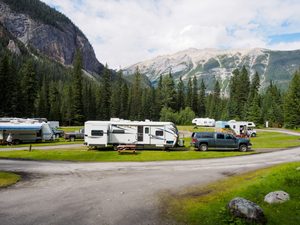 Catskill Mountains, NY: Hiking, Camping & Nature Adventures 4 RV campground surrounded by dense evergreen forest and dramatic mountain scenery, with travel trailers, vehicles, picnic tables, and grassy campsites.