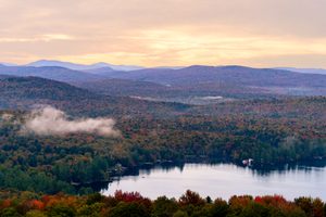 Adirondack Park, NY: A Wilderness Adventure of Mountains, Lakes 1 Panoramic view of a peaceful lake surrounded by colorful autumn forests and rolling mountains beneath a soft pastel sunset sky in the Adirondack region of New York.