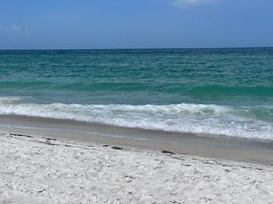 Quiet white-sand beach with gentle turquoise ocean waves rolling onto the shoreline beneath a clear blue sky.