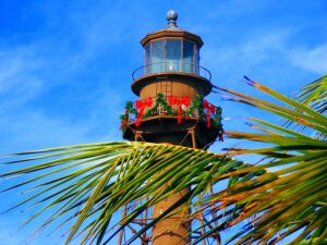A lighthouse and palm trees on a blue-sky day.