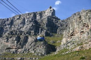 Tall mountains with rock walls and a cable car for visitors with green vegetation on a clear blue-sky day.
