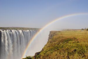Waterfalls with a rainbow in a rainforest with steep cliffs and a blue sky.