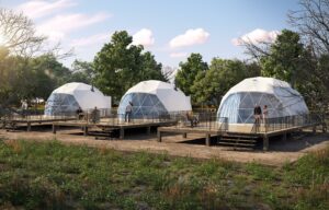 People at three glamping domes on platforms with stairs and a porch with trees and grass.