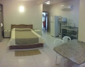 Room with bed and a rug with as table and chairs with a refrigerator. 