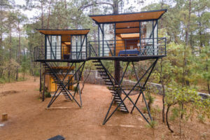 Boutique Treehouses in Embu Das Artes: Glamping with Artistic Charm 1 Two tall structures elevated elevated in a forest.
