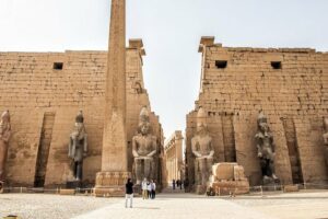 People standing at a temple with tall walls and several statues and an obelisk.