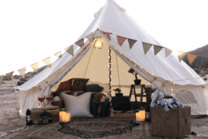 Oceanfront glamping tent decorated with large pillows, plants, candles, and small holiday lights.
