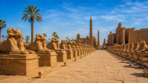 Karnak Temple – Luxor, Egypt: Gateway To Ancient Wonders 16 Avenue of Sphinxes near Karnak Temple in Luxor, Egypt, featuring long rows of ancient sphinx statues, palm trees, obelisks, and sandstone temple ruins.