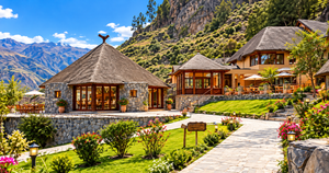 Colca Canyon Eco Retreat – Sustainable Glamping in the Andes 1 Beautiful daytime view of an Andean-style eco-lodge near Colca Canyon, Peru, featuring traditional stone buildings, thatched roofs, landscaped gardens, colorful flowers, stone walkways, outdoor dining terraces, and spectacular mountain scenery beneath a bright blue sky.