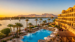 Karnak Temple – Luxor, Egypt: Gateway To Ancient Wonders 3 Luxury hotel overlooking the Nile River in Luxor, Egypt, featuring a swimming pool, palm trees, sailboats, and desert mountains at sunset.