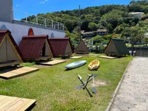 Jungle cabins with canoes in front with paddles and a sidewalk and trees in the background.