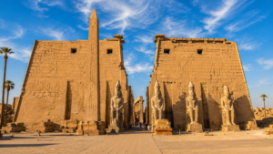 Karnak Temple – Luxor, Egypt: Gateway To Ancient Wonders 8 Monumental pylons at Karnak Temple in Luxor, Egypt, featuring towering sandstone walls, ancient carvings, an obelisk, pharaoh statues, and palm trees.