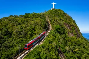 ✨ Rio De Janeiro Glamping Hub: Luxury Nature Stays in Brazil’s Most Vibrant City 11 Red Corcovado train climbing through lush green rainforest toward the Christ the Redeemer statue atop Corcovado Mountain in Rio de Janeiro, Brazil.